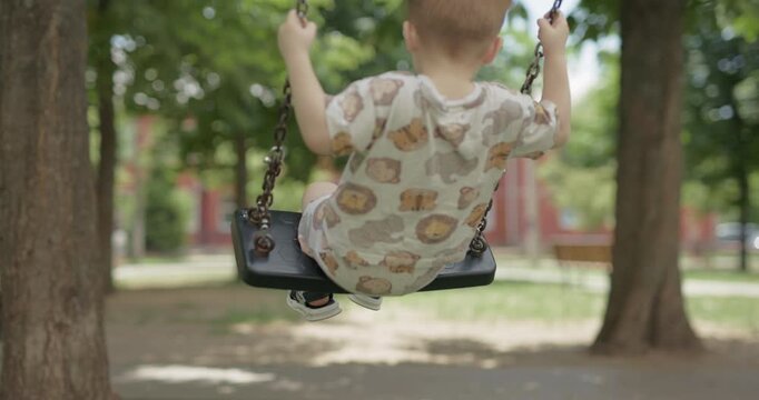 Cute young kid having fun on chain swing at outdoor play yard, slow motion