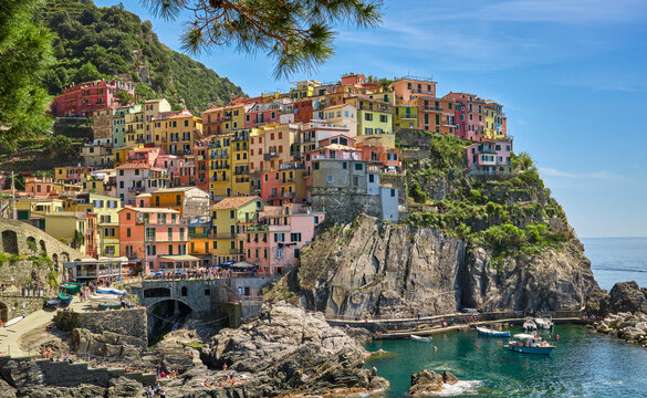 Colorful houses cascade down the cliffs of Riomaggiore in Cinque Terre, Liguria, Italy. Scenic coastal village with historic architecture, rocky shoreline, turquoise sea and Mediterrane atmosphere