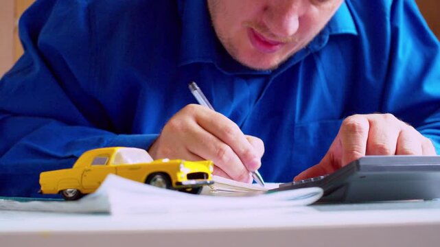 Car insurance agent carefully writing in document at desk close up. Focus on hands and pen, yellow toy car on table. Shallow depth of field, natural light. Businessman filling automotive policy