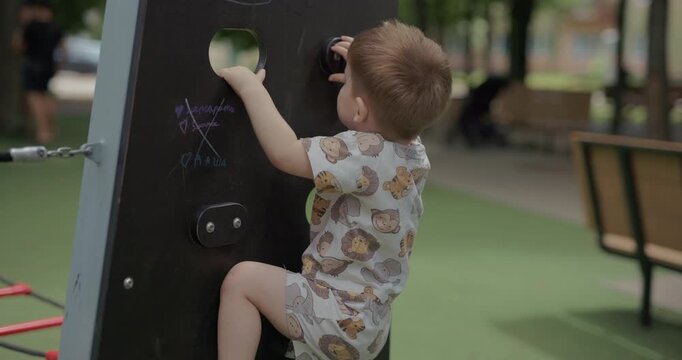 Little toddler boy climbing up a small climbing wall on playground, slow motion