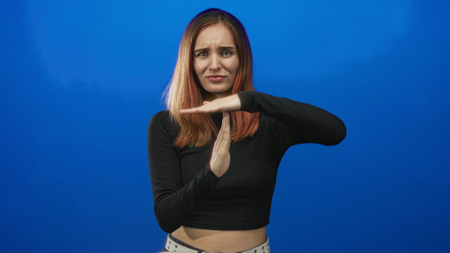Woman making timeout gesture with hands and exposed waist against blue studio backdrop; concern pause boundary.