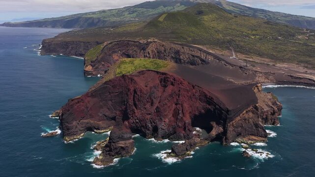 Aerial view of the dramatic volcanic landscape of Capelinhos with its dark red cliffs and rugged coastline meeting the Atlantic Ocean in Capelo, Azores, Portugal.