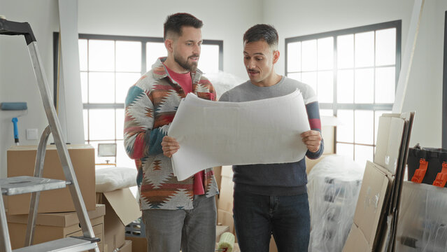 Man holding blueprint with both hands and reading plan in an apartment full of boxes and ladder; home planning anticipation.