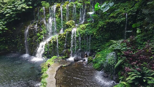 Woman on scenic tropical waterfall surrounded by rainforest greenery