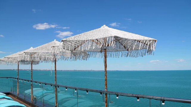 Beautiful row of bohemian style umbrellas with fringe on a sunny rooftop terrace, offering a breathtaking panoramic view of the turquoise ocean horizon in the distance