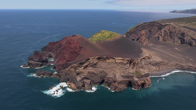Aerial view of the volcanic landscape of Capelinhos with rugged cliffs, dark volcanic soil, and green vegetation surrounded by the Atlantic Ocean in Capelo, Azores, Portugal.