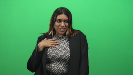 Fototapeta premium Woman touching hand to chest in green screen studio wearing patterned top and blazer; shyness authenticity.