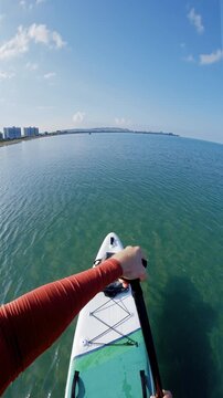 First person view on stand up paddle board gliding over turquoise ocean near coastal city buildings