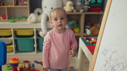 Little blonde girl reaches into toy bin and touches easel in a playroom building  playful curiosity. © Krakenimages.com