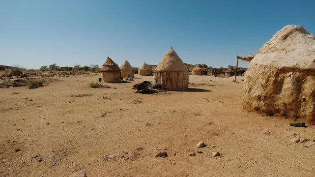 Traditional himba settlement with mud huts in the arid landscape, namibia, under a clear blue sky