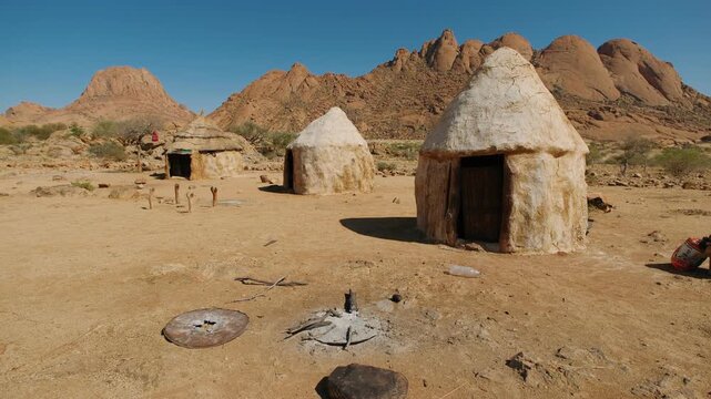 Traditional african village with mud huts in the arid landscape of namibia. The iconic spitzkoppe mountains rise in the background