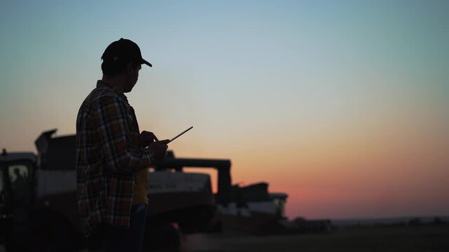 Agriculture. Agronomist in wheat field with clipboard at sunset. Harvester cleans wheat field. Farmer agronomist in wheat field controls harvesting. harvester silhouette at sunset. Harvesting wheat