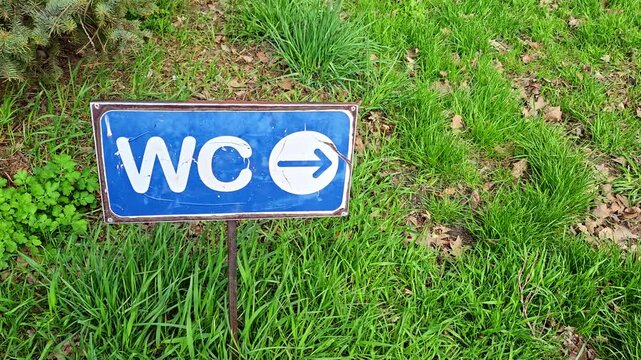 Blue pointer sign with toilet icon indicating direction on green grass