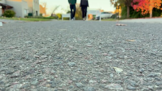 Low angle shot of a man and a woman in sneakers walking towards the camera on an asphalt street during autumn, young couple, Argentina