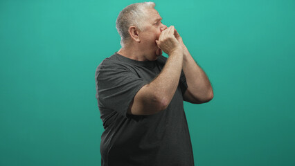 Fototapeta premium Senior man cupping hands to mouth shouting in studio with teal wall, visible bare hands and forearms in profile calling out to distance; communication urgency.