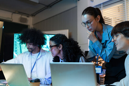Tech team analyze code on laptop computer at night. Serious woman metor watching colleague to check digital screen for software update and startup corporate project