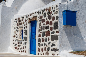 Traditional Cycladic facade with blue door, white plaster and volcanic stone wall in Santorini, Greece, captured in bright summer light. © Andrei Tomas
