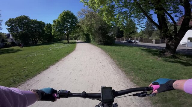 POV ride on an electric mountain bike through a city park in Munich Germany. Cyclist perspective with gravel trail, trees and outdoor recreation showing modern sustainable transportation.