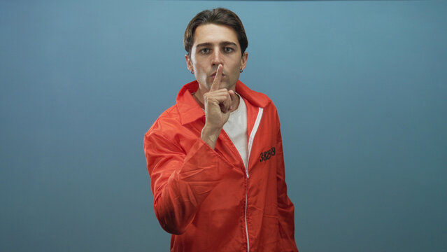 Man points finger at camera wearing orange prisoner jumpsuit with visible inmate number in studio; accusation.