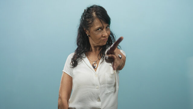 Woman senior points index finger to camera in studio wearing white blouse and pendant showing scolding gesture; warning.