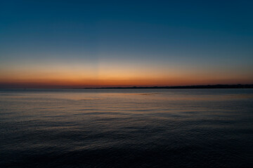 Obraz premium Serene panoramic view of Lake Constance after sunset, featuring a clear twilight sky with a vibrant orange glow on the horizon fading into deep blue