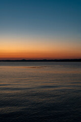 Obraz premium Serene panoramic view of Lake Constance after sunset, featuring a clear twilight sky with a vibrant orange glow on the horizon fading into deep blue