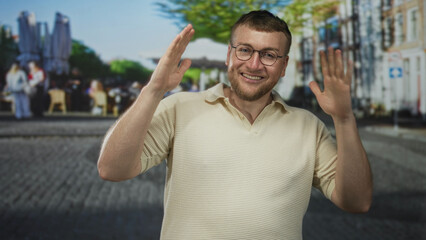 Fototapeta premium Man raising hands on a cobblestone street smiling and looking upward with glasses and beard; joy celebration.