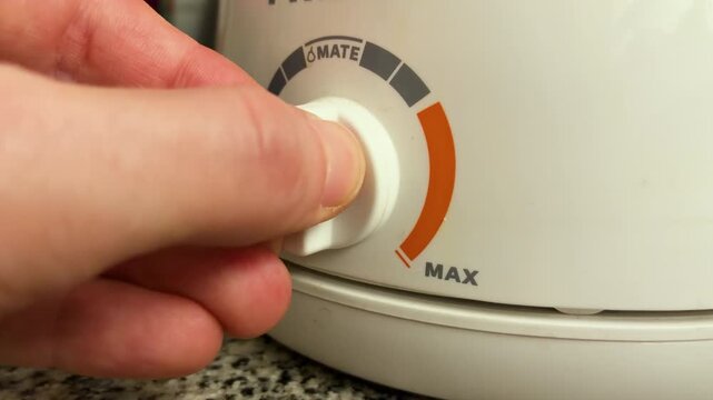 Hand turning temperature knob on electric kettle to precise yerba mate water setting before boiling, traditional Argentine beverage