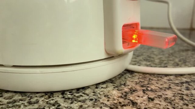Close up of hand pressing electric kettle power switch turning on orange red indicator light