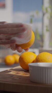 Hand wipes orange with paper towel on kitchen counter with fresh oranges nearby. Concept of citrus recipe preparation and homemade cooking