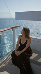 Obraz premium Woman sitting with clasped hands on cruise terrace bench overlooking ocean wake and glass railing, wearing dark dress and necklace; serenity.
