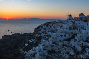 Whitewashed cliffside houses and windmill overlooking the Aegean Sea at dusk in Santorini, Greece. © Andrei Tomas