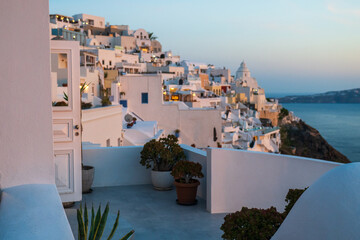 Traditional Cycladic architecture overlooking the Aegean Sea in Oia, Santorini, during golden hour with pastel sky and terraced buildings. © Andrei Tomas