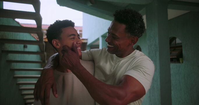 Father and teenage son of African descent standing together arm in arm in a corridor smiling and enjoying a strong family bond