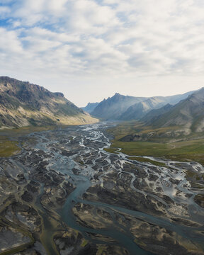 Aerial view of Kol-Suu lake and its braided river system flowing through a dramatic mountain valley with rocky slopes and soft clouds At-Bashi District, Naryn Region, Kyrgyzstan.
