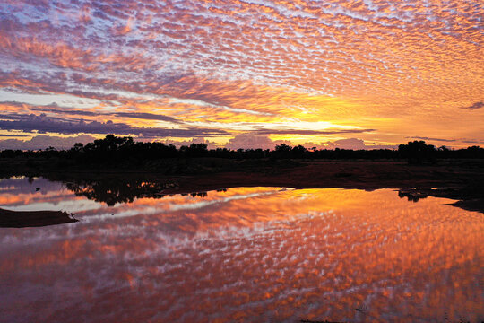 Aerial view of a vibrant sunset reflecting over a calm water body in the outback landscape of Jundah, Queensland, Australia.