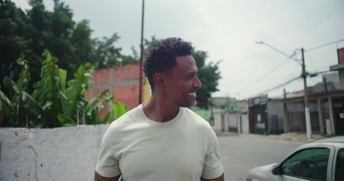 Man of African descent smiling warmly while standing on a quiet street in a South American urban city, cheerful and relaxed, surrounded by greenery and buildings
