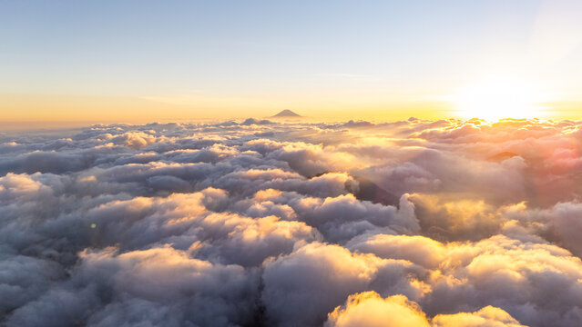 Aerial view of a mountain peak rising above a dense layer of clouds during golden hour with warm sunlight illuminating the sky Indonesia.