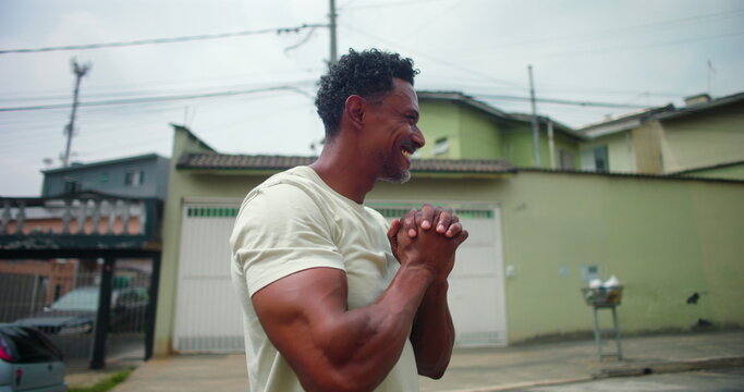Man of African descent in an urban street, hands clasped in prayer, looking upward with a peaceful expression, symbolizing spirituality, hope, and devotion