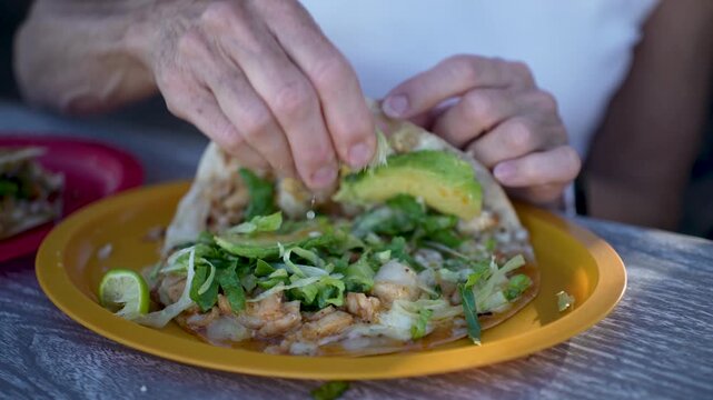 A senior woman enjoys squeezing fresh lime on her fish and shrimp tacos at a taco stand in Baja California Mexico for a tasty meal.