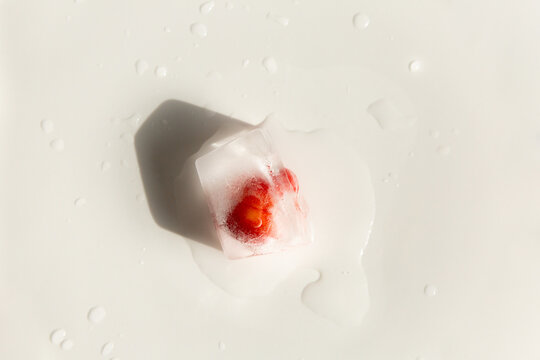 Gla&ccedil;on givr&eacute; avec une cerise rouge &agrave; l'int&eacute;rieur, pos&eacute; sur un fond blanc avec un &eacute;clairage vif et lumineux, gros plan vue du dessus, flaque d'eau et gouttelettes, ambiance de fra&icirc;cheur 