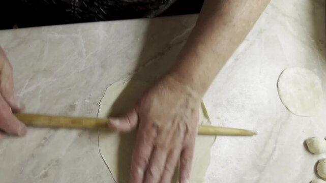 Cook rolling out flatbread dough with thin wooden pin on kitchen counter top