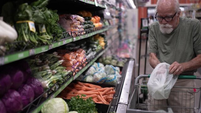 Senior man picks fresh fruits and vegetables in a grocery store while enjoying his shopping experience.
