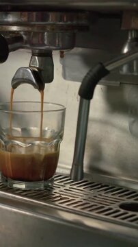 Vertical video: Starting espresso group head pouring two jets into glass on counter, finishing shot