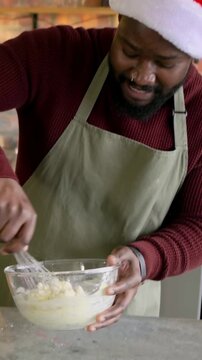 Vertical video: Whisking man in Santa hat and green apron at counter, checking tablet, copy space