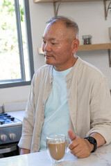 Senior Asian man holding double-walled glass mug and looking left at kitchen countertop window © wavebreak3