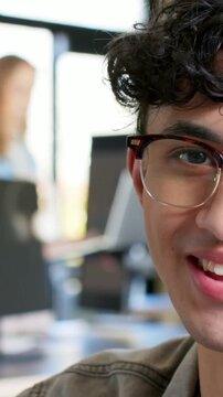 Vertical video: Looking down then up, guy in tortoise specs smiling then laughing at peer in office
