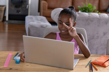 Obraz premium African American girl child wearing pink top sitting at table in living room using silver laptop
