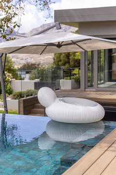 White inflatable donut float is floating near pool edge in modern backyard, umbrella shading deck