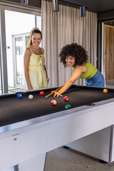 Naklejka premium Diverse female friends playing pool in rec room, leaning over black-felt table using cue stick